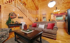 Cozy cabin-style interior with a wooden staircase, comfortable living room, and a kitchen area.