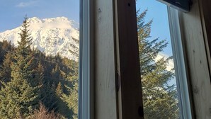 Une vue à travers une fenêtre à cadre en bois, donnant sur un paysage enneigé avec une montagne en arrière-plan.