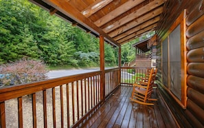 Une véranda en bois avec une balustrade en bois, une chaise berçante et une vue sur une zone boisée.