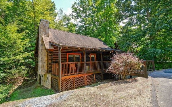 Une cabane rustique avec une cheminée en pierre, une terrasse en bois et un porche abrité.