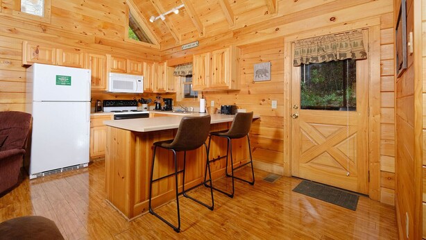 Una cabaña de madera con cocina equipada con refrigerador, microondas, estufa y taburetes de bar.