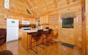 Une cabane en bois dotée d’une cuisine équipée d’un réfrigérateur, d’un four à micro-ondes, d’une cuisinière et de tabourets de bar.