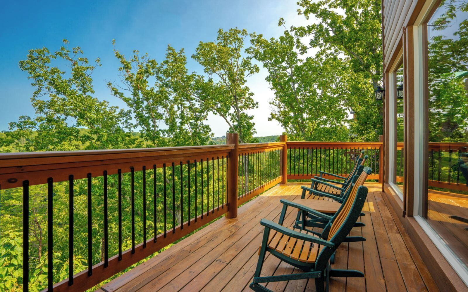 Eine Holzterrasse mit Geländer, einer Reihe von Stühlen und Blick auf einen Wald.
