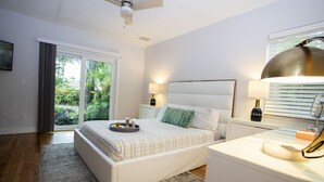 A modern bedroom with a large bed, bedside lamps, a ceiling fan, and a view of greenery through the sliding glass door. - 4BR, Private Backyard Oasis/POOL & HotTub(Jacuzzy) (Hollywood)