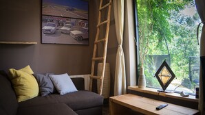 A living room with a sofa, a wooden ladder, a window with a view of trees, and a painting on the wall. - Bright duplex apartment, surrounded by pine forest, pets welcome (Torrellas de llobregat)