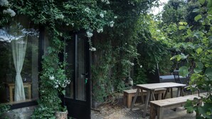 A patio area with a stone floor, wooden furniture, and a black door. - Bright duplex apartment, surrounded by pine forest, pets welcome (Torrellas de llobregat)