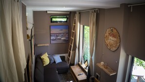 A cozy living room with a sofa, a TV mounted on the wall, a ladder, and a window with curtains. - Bright duplex apartment, surrounded by pine forest, pets welcome (Torrellas de llobregat)