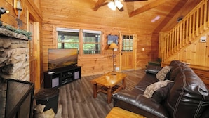 A cozy log cabin interior with a stone fireplace, a leather sofa, a wooden coffee table, and a television on a wooden stand. - Heaven on Earth - Pet Friendly & Secluded (Sevierville)