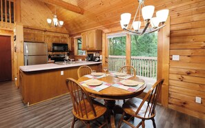 A wooden cabin kitchen with a dining table set for four, a refrigerator, stove, and microwave.
