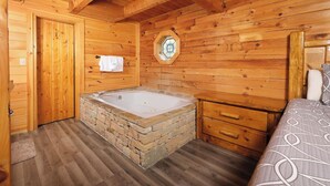 A wooden cabin interior with a stone bathtub, wooden walls, a wooden door, and a bed with patterned bedding. - Heaven on Earth - Pet Friendly & Secluded (Sevierville)