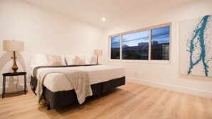Un dormitorio con una cama, dos mesitas de noche, una ventana y un cuadro en la pared.