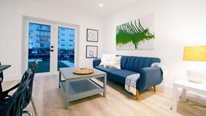 Una sala de estar moderna con un sofá azul, una mesa de centro y vistas a un edificio a través de puertas de vidrio.