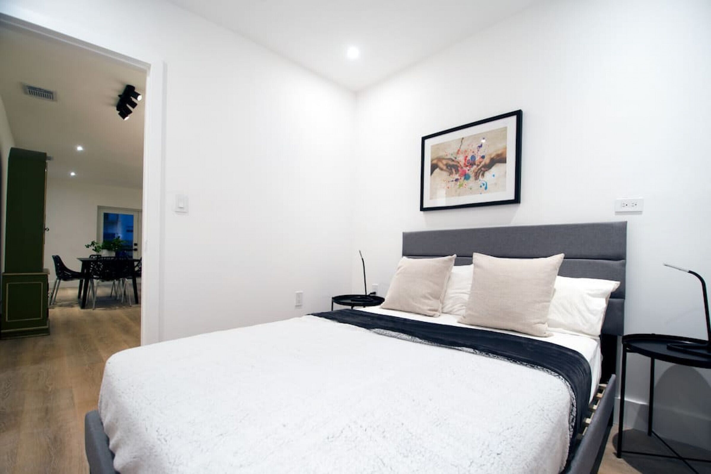 Ein modernes Schlafzimmer mit einem großen Bett, einem Nachttisch und einem gerahmten Kunstwerk an der Wand.