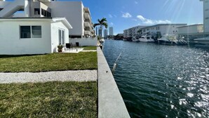 Una propiedad frente al agua con un edificio blanco moderno, un área verde y un camino de hormigón que conduce al agua.
