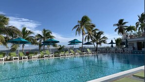A pool area with lounge chairs and umbrellas, surrounded by palm trees. - Waterfront Bring Your Boat Cabana Club Membership Included (Key Colony Beach)