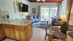A spacious living area with a wooden ceiling, a TV mounted on the wall, and a dining area with a glass table and chairs. - Waterfront Bring Your Boat Cabana Club Membership Included (Key Colony Beach)