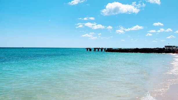 A beach with clear turquoise water, a sandy shore, and a pier extending into the water. - Waterfront Bring Your Boat Cabana Club Membership Included (Key Colony Beach)