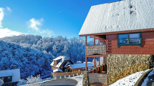 A chalet with a stone facade, wooden balcony, and a view of snow-covered trees. - Above It All - Pet Friendly, 3 Mi to Dollywood, Hot Tub + Pool Table & Games (Sevierville)
