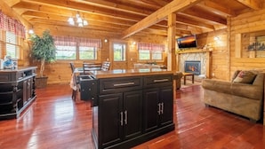 A spacious living area with a wooden ceiling, a fireplace, a television, and a dining area with a table and chairs. - Above It All - Pet Friendly, 3 Mi to Dollywood, Hot Tub + Pool Table & Games (Sevierville)