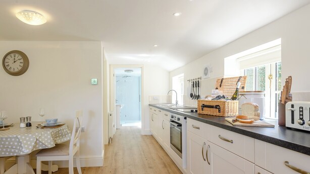 A modern kitchen with white cabinetry, a dining table with a polka dot tablecloth, and a clock on the wall. - 1 bedroom accommodation in Fulletby, near Horncastle (Fulletby, near Horncastle)
