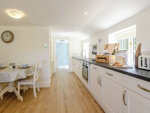 Une cuisine moderne avec des meubles blancs, une table à manger recouverte d’une nappe à pois et une horloge au mur.