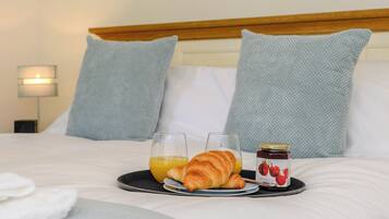 Ein ordentlich bezogenes Bett mit einem Tablett Frühstücksgebäck, darunter Croissants, Orangensaft und Marmelade.