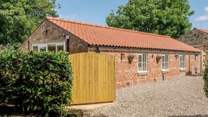 Een bakstenen gebouw met een rode dakbedekking, een houten poort en een grindpad.