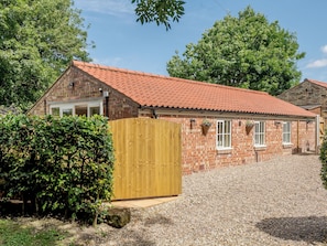A brick building with a red-tiled roof, a wooden gate, and a gravel driveway.