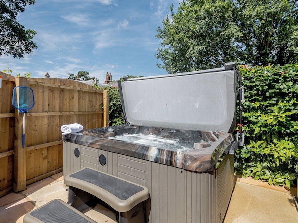 Un bain à remous avec un banc, une clôture en bois et de la verdure en arrière-plan.