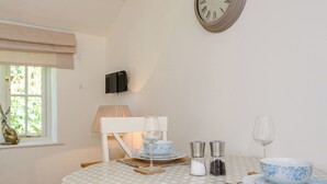 Een eettafel met een tafelkleed met stippen, een klok aan de muur, een raam met uitzicht en een lamp.