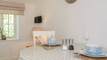 A dining table with a polka dot tablecloth, a clock on the wall, a window with a view, and a lamp.