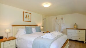Een slaapkamer met een bed, nachtkastjes, een kaptafel, een dressoir, een spiegel en een schilderij aan de muur.