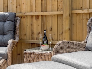 Des meubles en osier, une bouteille de vin et un verre sur une table.