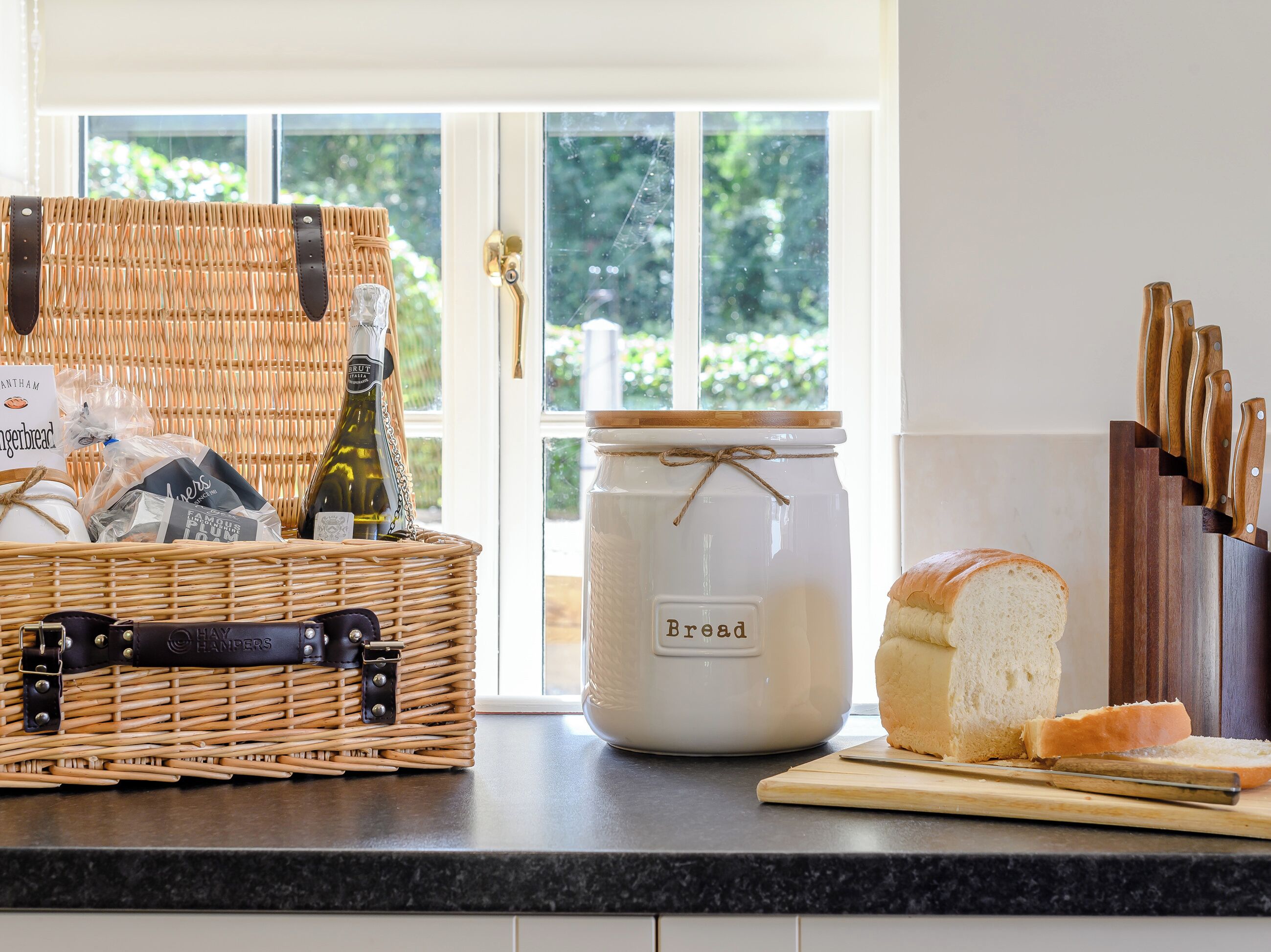 Un plan de travail de cuisine avec un panier en osier, un pot à pain, une miche de pain et un bloc à couteaux.