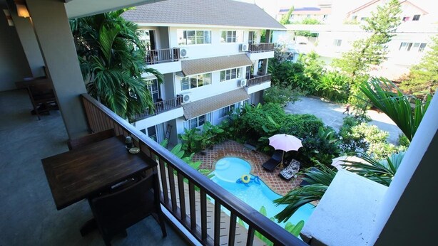 A balcony with a view of a swimming pool, surrounded by lush greenery and a multi-story building in the background. - The Opium Serviced Apartment and Hotel (Chiang Mai)