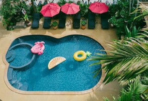 Piscina con sillas de descanso y sombrillas, rodeada de plantas en macetas.