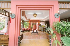 Un vestíbulo con un arco rosa, un jarrón central y una zona de estar con sofá y sillones.