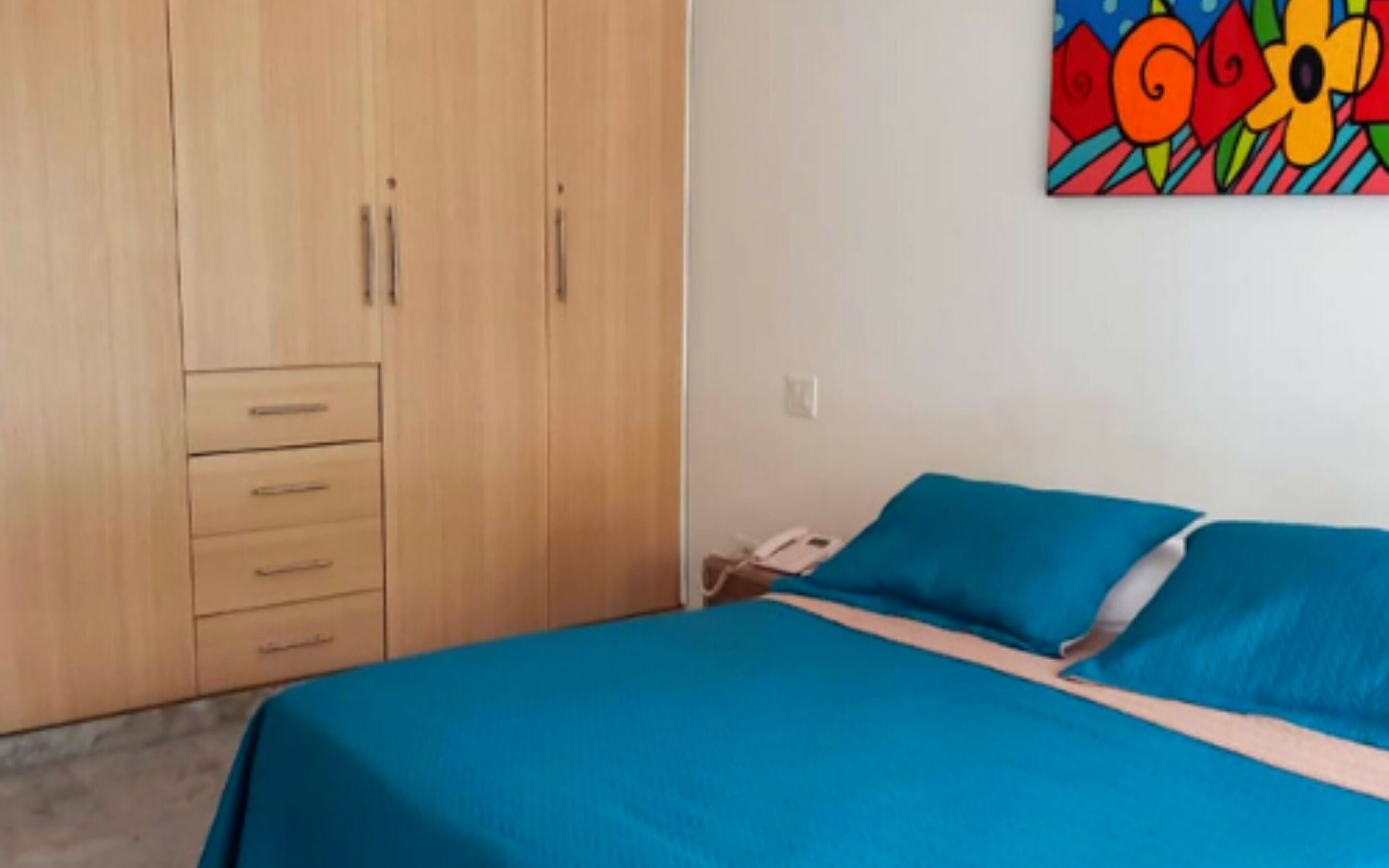 Ein Schlafzimmer mit einem Bett, einem Kleiderschrank und einem farbenfrohen Bild an der Wand.
