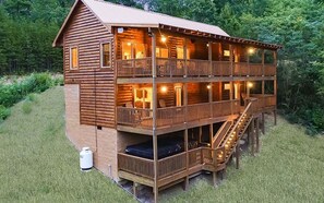 A two-story log cabin with a balcony on the upper floor, a staircase leading to the upper level, and a small outdoor area with a water heater.