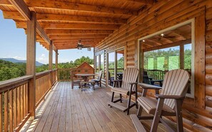 A wooden deck with Adirondack chairs and a table, overlooking a scenic landscape.
