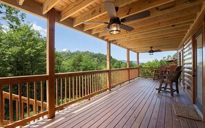 A wooden deck with a railing, ceiling fans, and outdoor furniture.