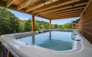 A hot tub under a wooden pergola with a view of a forested area.