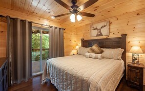 Ein Schlafzimmer einer Holzhütte mit Bett, Vorhängen, Deckenventilator und Hirschbild.