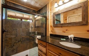 A bathroom with a stone wall, a wooden vanity, a sink, and a mirror.