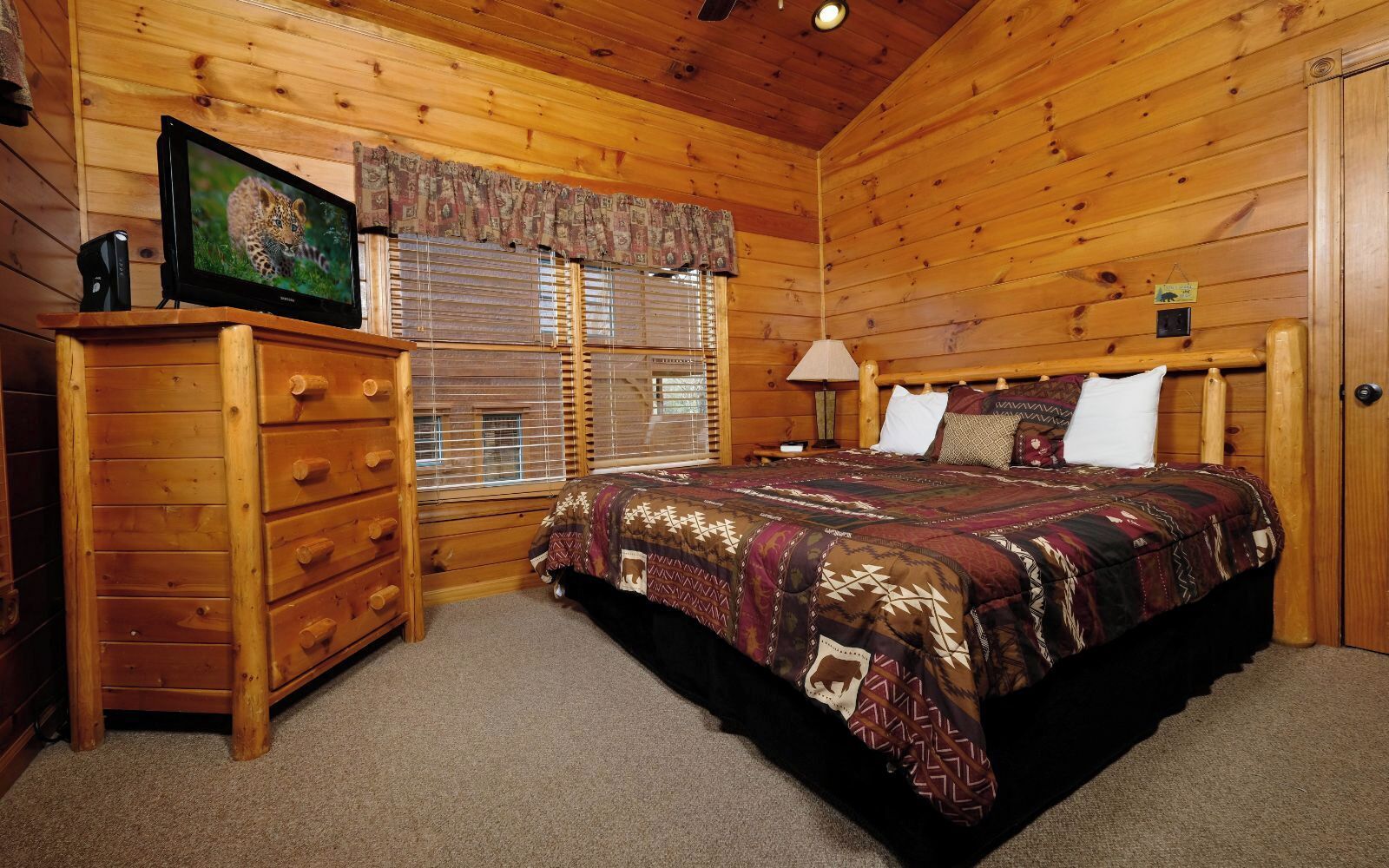 A wooden cabin bedroom with a bed, dresser, and a television displaying a leopard.