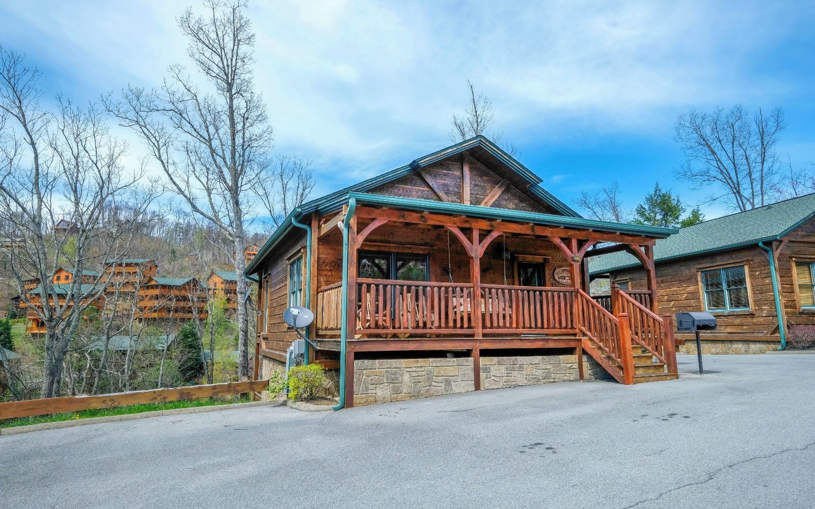 A wooden lodge with a porch, stone foundation, and a view of surrounding trees and mountains.