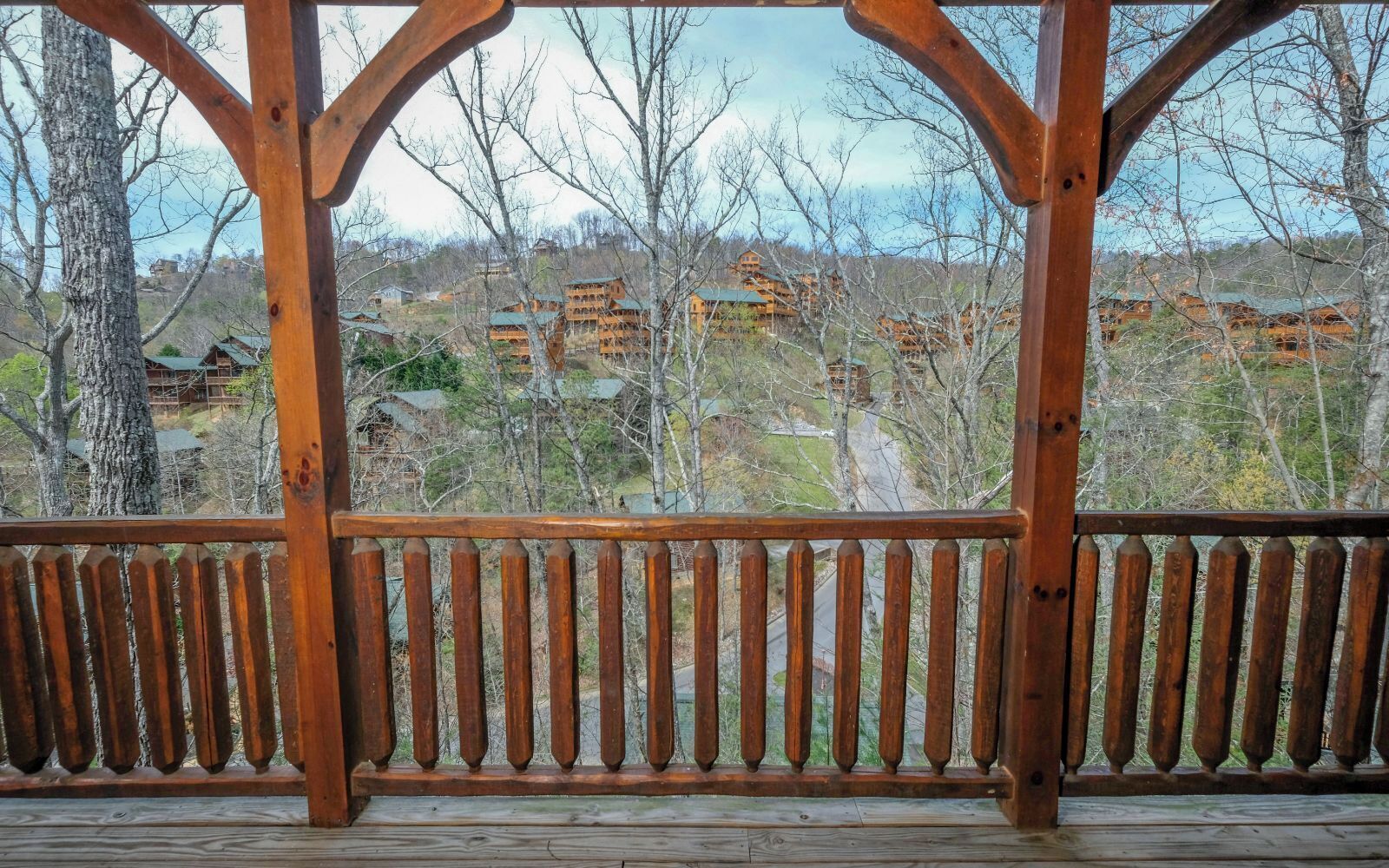 A wooden deck with a railing, overlooking a residential area with houses and trees.