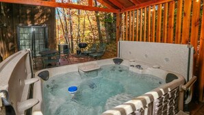A hot tub with a wooden deck and a view of a forest.