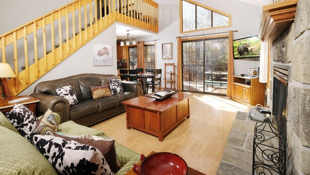 A spacious living room with a wooden staircase, a fireplace, and a large sliding glass door leading to an outdoor patio.