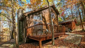 A rustic cabin with a wooden deck and a stone pathway leading to the entrance.